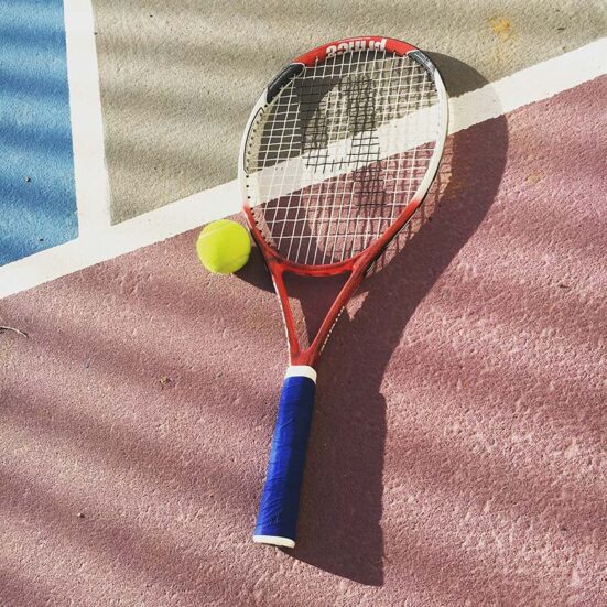 Ein Tennisball und Tennisschläger liegen auf einem Spielfeld.